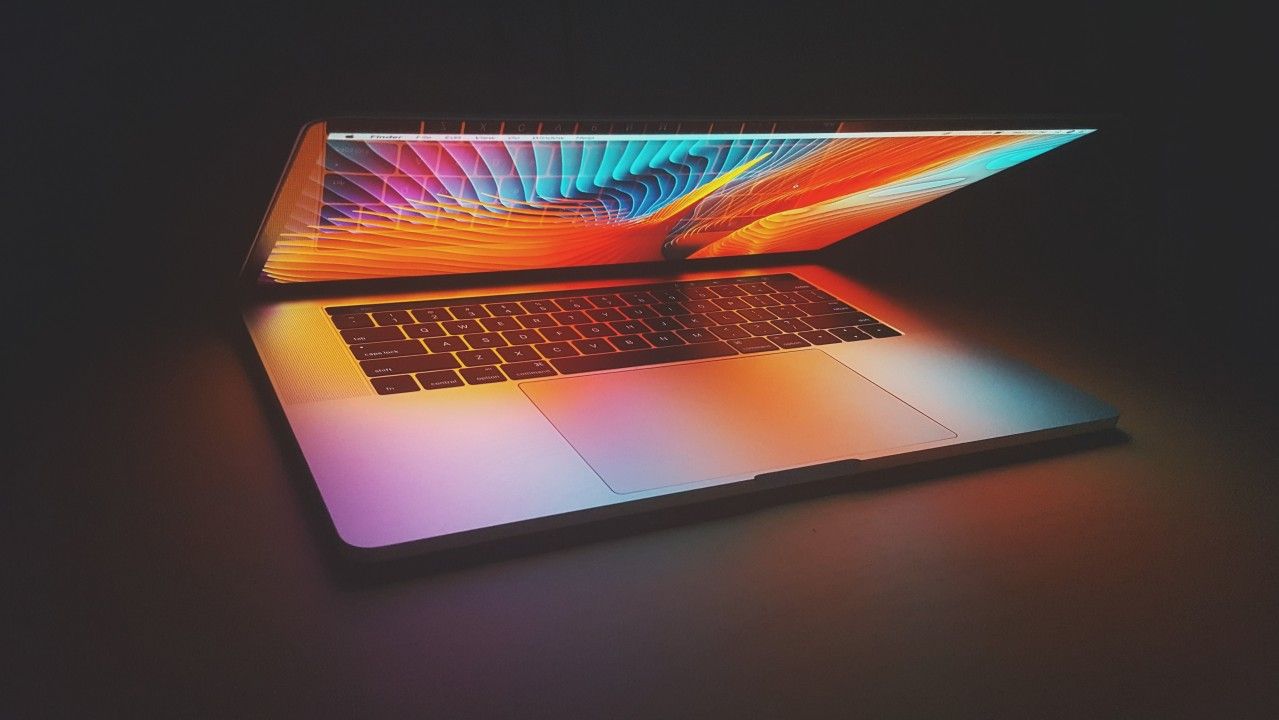 Half closed macbook pro with an orange, blue and pink wavy background and the keyboard reflecting on the screen.